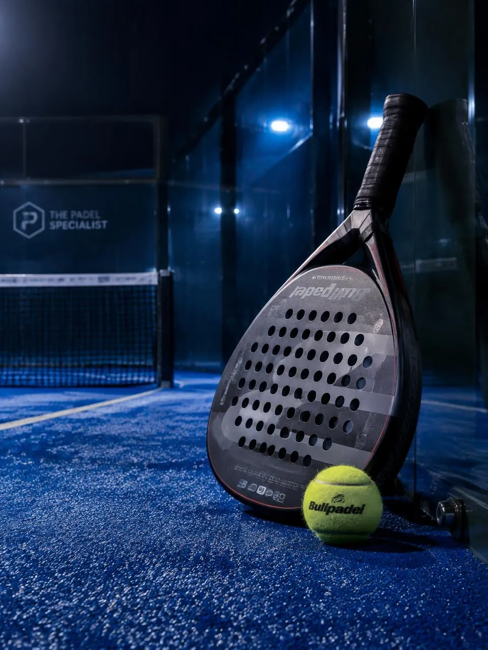 Padelmaila ja pallo padelkentän tekonurmella lasiseinän vieressä