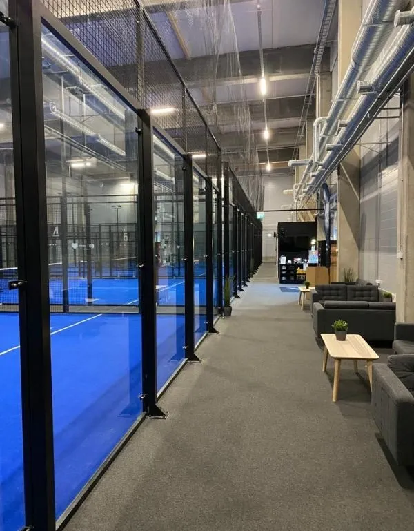 Käytävä padelkenttien lasiseinän vieressä, oleskelualue taustalla